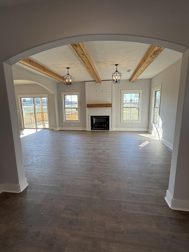 unfurnished living room with a fireplace, a wealth of natural light, beamed ceiling, and dark wood-type flooring