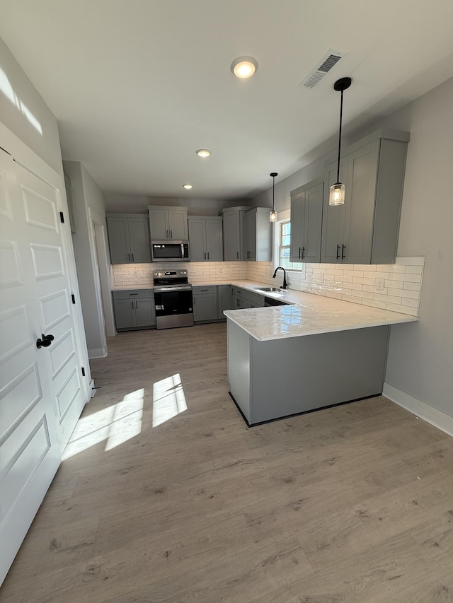 kitchen featuring kitchen peninsula, hanging light fixtures, gray cabinets, appliances with stainless steel finishes, and sink