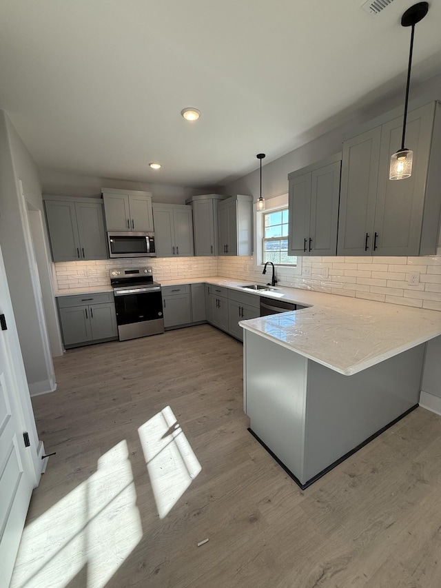 kitchen featuring kitchen peninsula, pendant lighting, gray cabinets, appliances with stainless steel finishes, and sink