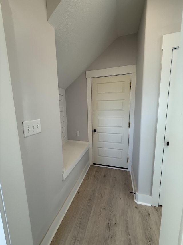 corridor featuring a textured ceiling, light hardwood / wood-style floors, and lofted ceiling