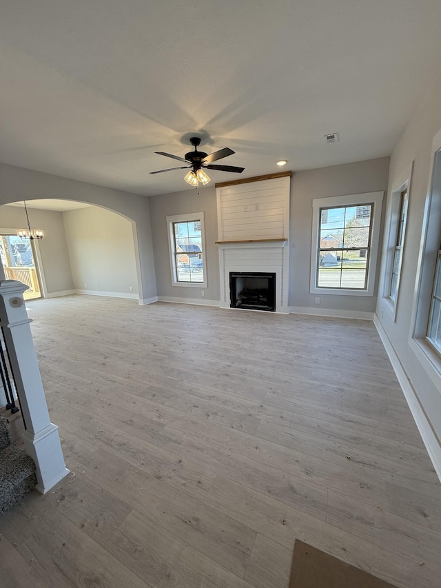 unfurnished living room with ceiling fan with notable chandelier, a fireplace, light hardwood / wood-style flooring, and a wealth of natural light