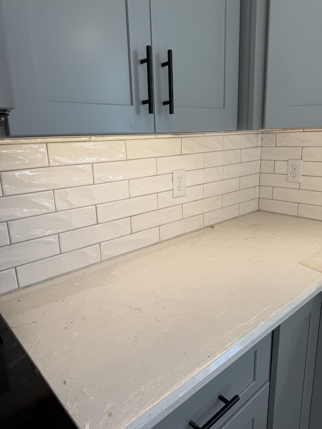 interior details with decorative backsplash, light stone counters, and gray cabinets