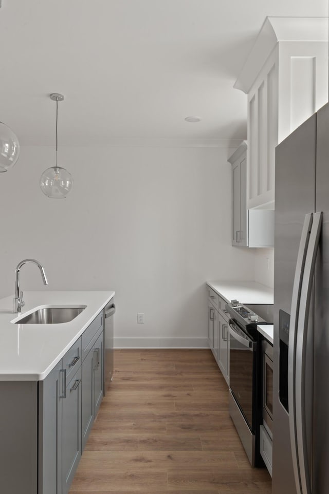 kitchen featuring sink, light hardwood / wood-style floors, gray cabinets, pendant lighting, and appliances with stainless steel finishes