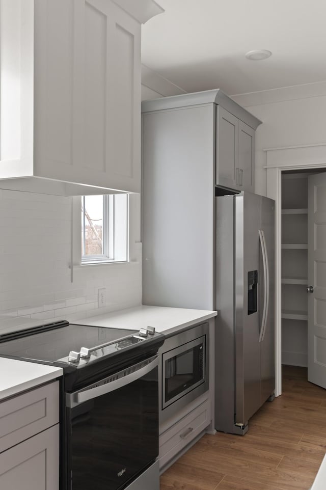 kitchen featuring decorative backsplash, light wood-type flooring, crown molding, gray cabinetry, and appliances with stainless steel finishes