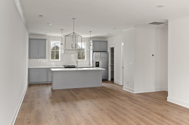 kitchen with tasteful backsplash, an island with sink, gray cabinets, stainless steel refrigerator with ice dispenser, and pendant lighting