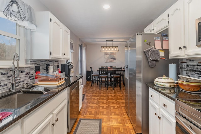 kitchen with appliances with stainless steel finishes, dark stone counters, pendant lighting, white cabinets, and sink