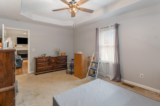 carpeted bedroom with ceiling fan and a raised ceiling