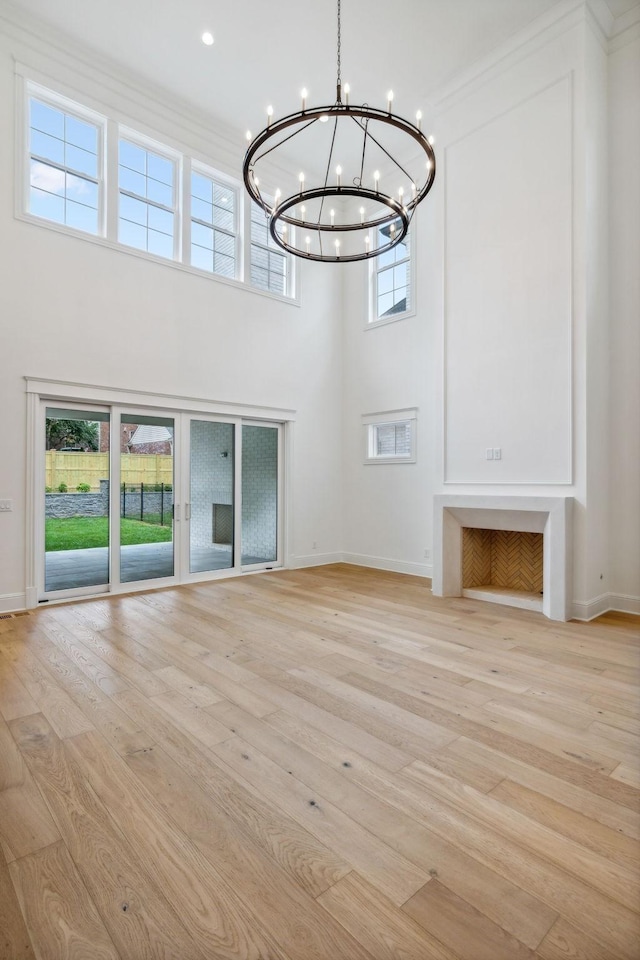 unfurnished living room featuring a towering ceiling, a chandelier, and light hardwood / wood-style floors