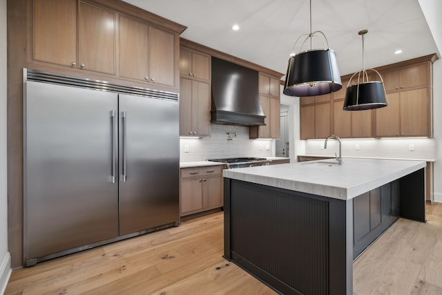 kitchen featuring sink, decorative light fixtures, custom range hood, light hardwood / wood-style flooring, and appliances with stainless steel finishes