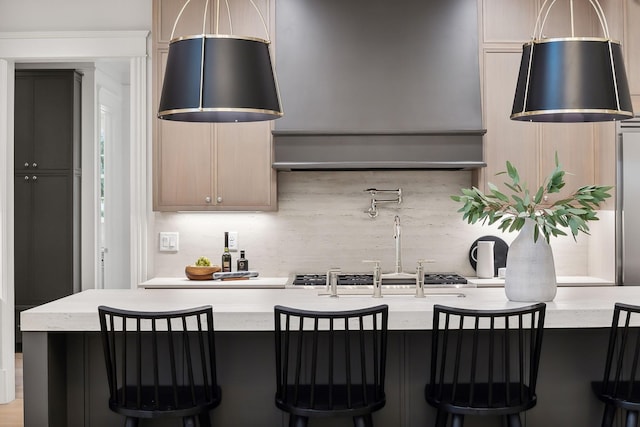 kitchen with light stone countertops, a kitchen island with sink, backsplash, and light brown cabinets