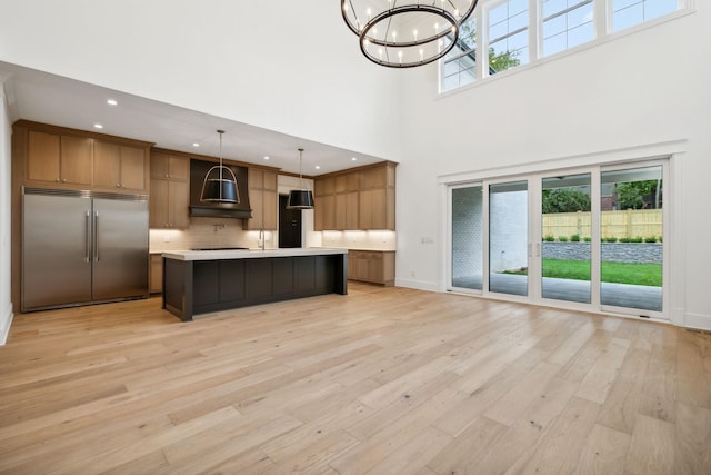 kitchen featuring a center island, stainless steel built in refrigerator, decorative backsplash, wall chimney range hood, and decorative light fixtures