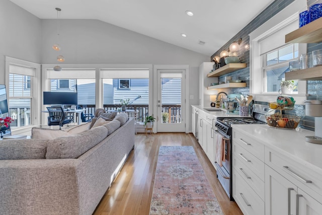 kitchen featuring sink, stainless steel gas range oven, hanging light fixtures, and white cabinetry