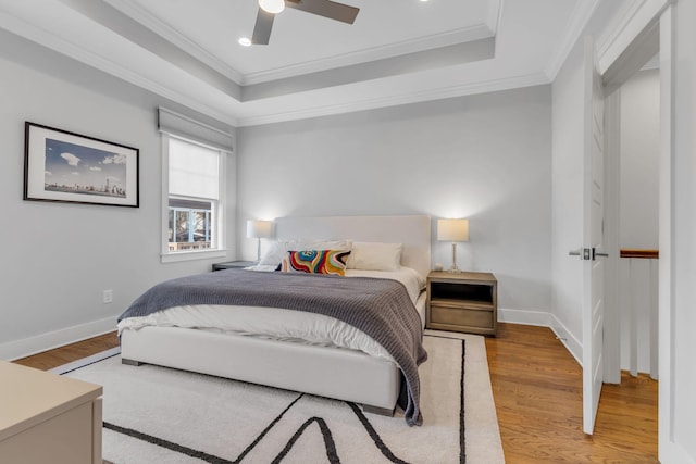 bedroom with ornamental molding, ceiling fan, light hardwood / wood-style flooring, and a tray ceiling