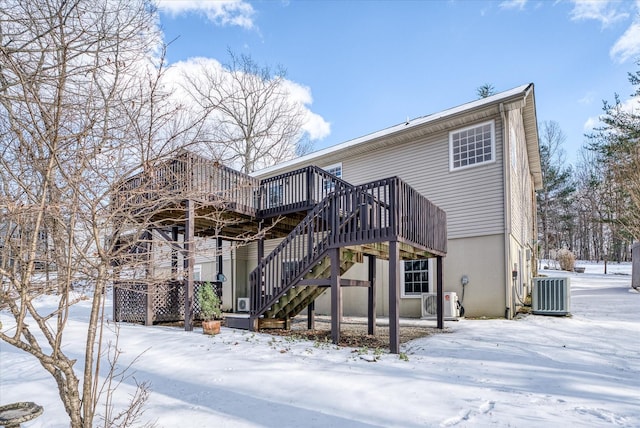 snow covered property with central air condition unit and a deck