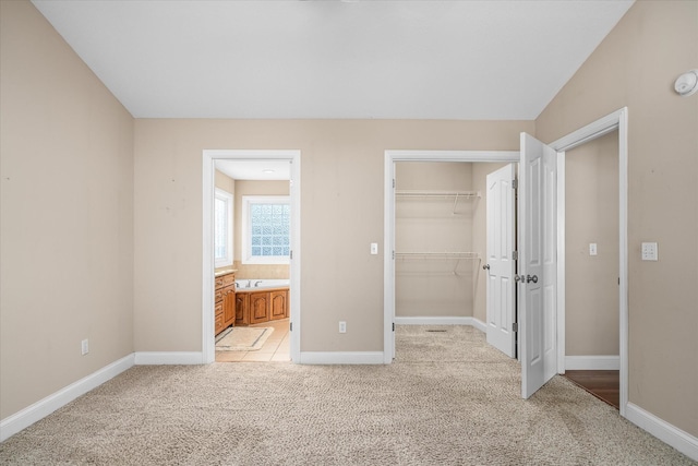 unfurnished bedroom with a walk in closet, ensuite bathroom, a closet, and light carpet