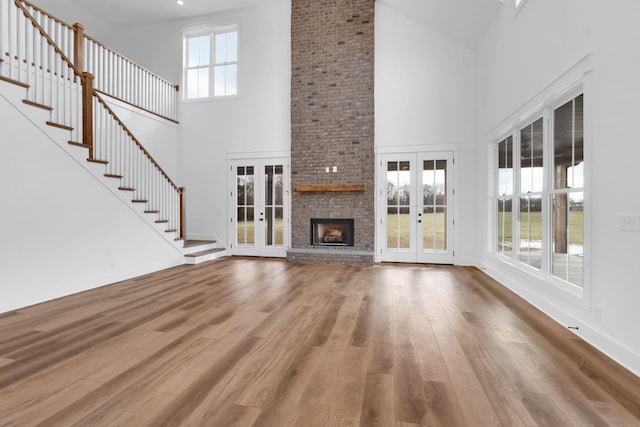 unfurnished living room with a towering ceiling, french doors, a brick fireplace, and hardwood / wood-style flooring