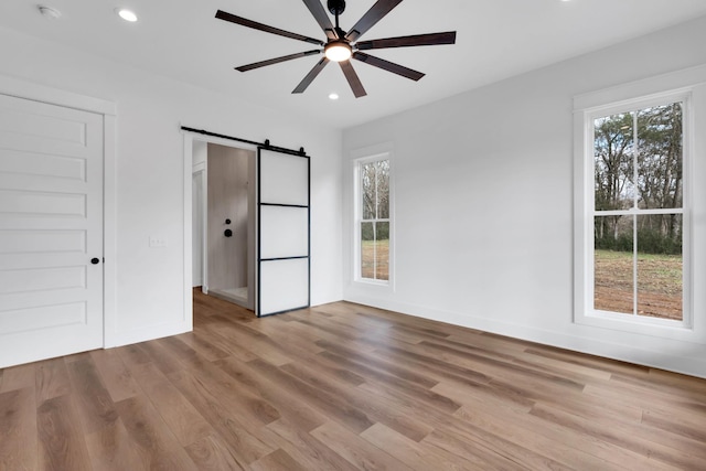 unfurnished bedroom with ceiling fan, a barn door, and light hardwood / wood-style floors