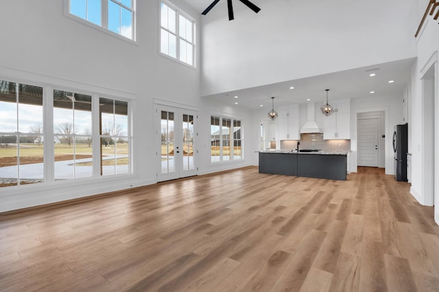 unfurnished living room with ceiling fan with notable chandelier, a high ceiling, and light hardwood / wood-style flooring