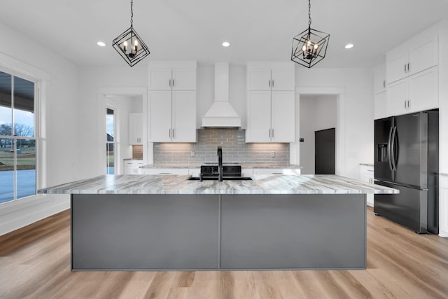 kitchen featuring light stone countertops, premium range hood, a spacious island, black appliances, and white cabinets