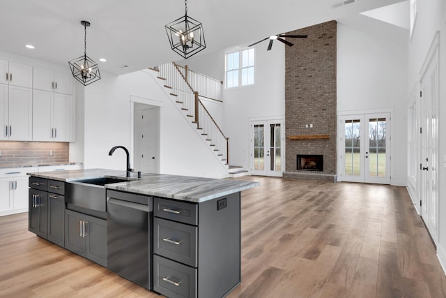 kitchen with stainless steel dishwasher, hanging light fixtures, an island with sink, french doors, and white cabinetry