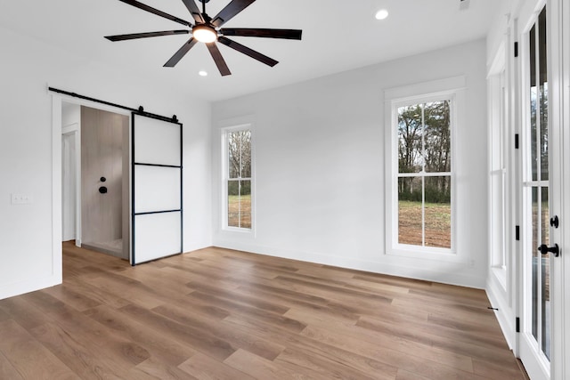 unfurnished bedroom with ceiling fan, a barn door, and light hardwood / wood-style floors