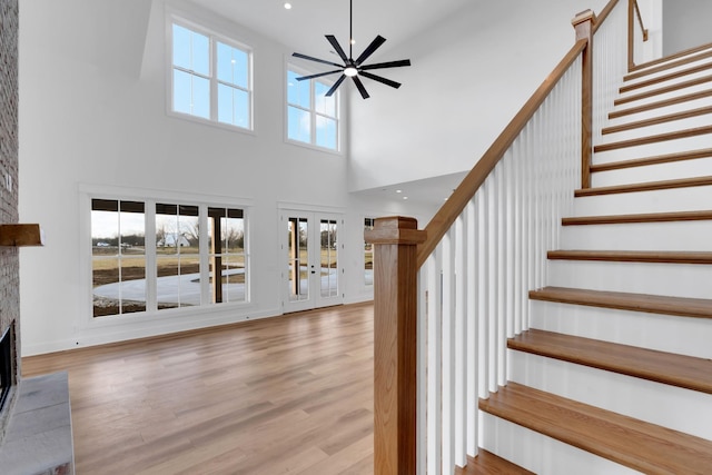 interior space with a fireplace, french doors, ceiling fan, light hardwood / wood-style floors, and a high ceiling