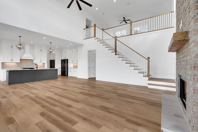 unfurnished living room with light wood-type flooring, a towering ceiling, and ceiling fan with notable chandelier