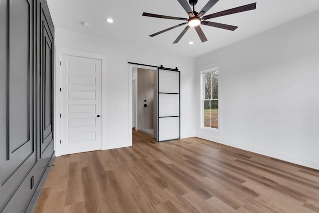 unfurnished bedroom with ceiling fan, light hardwood / wood-style floors, and a barn door