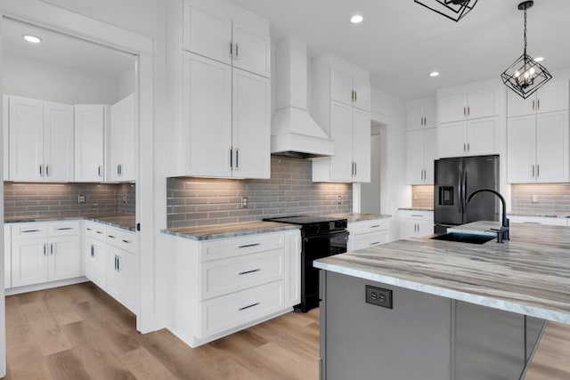 kitchen with white cabinets, premium range hood, black appliances, and decorative backsplash