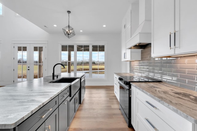 kitchen featuring an island with sink, white cabinetry, custom range hood, and black electric range oven