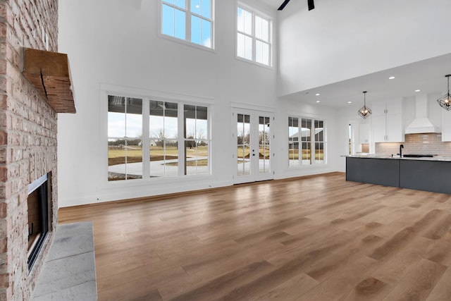 unfurnished living room with wood-type flooring, french doors, a fireplace, a high ceiling, and an inviting chandelier