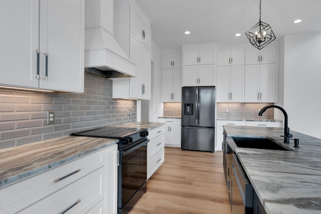 kitchen with black appliances, white cabinetry, and premium range hood