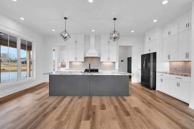 kitchen with a kitchen island with sink, custom range hood, light stone counters, white cabinets, and black fridge with ice dispenser