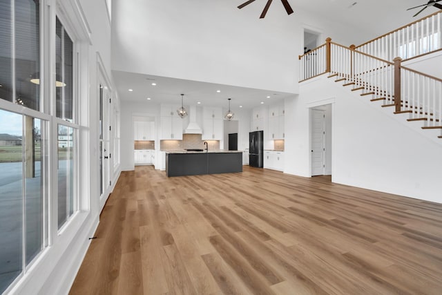 unfurnished living room featuring light hardwood / wood-style floors, sink, ceiling fan with notable chandelier, and a high ceiling