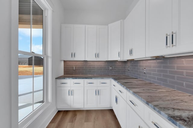 kitchen featuring white cabinets, dark stone counters, light wood-type flooring, and backsplash