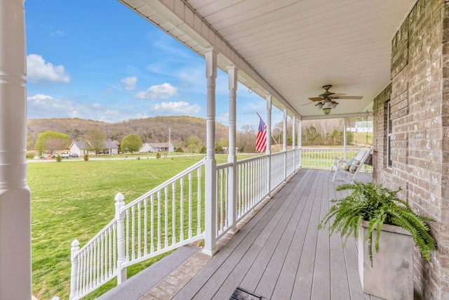 deck featuring a porch, ceiling fan, a yard, and a mountain view