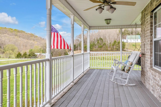 wooden deck featuring covered porch, ceiling fan, a yard, and a mountain view