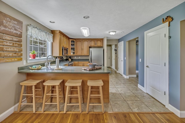 kitchen with appliances with stainless steel finishes, a kitchen breakfast bar, kitchen peninsula, and sink