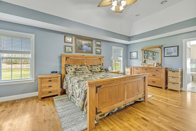 bedroom featuring ceiling fan, light hardwood / wood-style flooring, vaulted ceiling, and ensuite bath