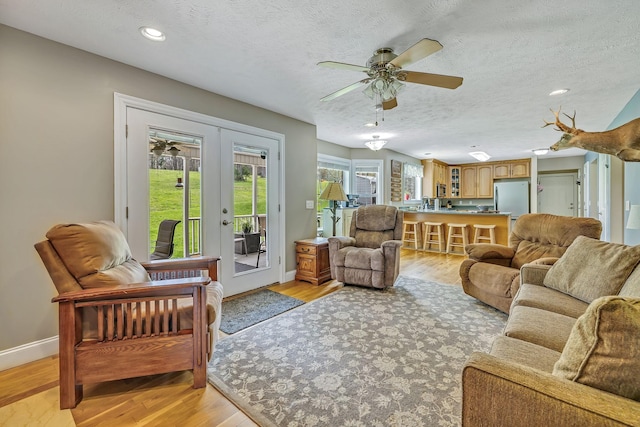 living room featuring a textured ceiling, light hardwood / wood-style flooring, french doors, and ceiling fan