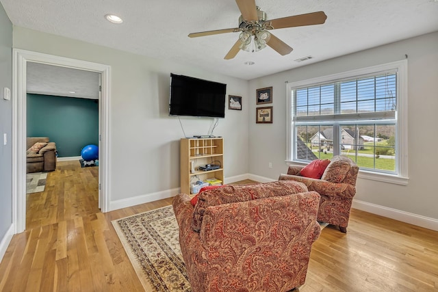 living room featuring light wood-type flooring, ceiling fan, and a textured ceiling