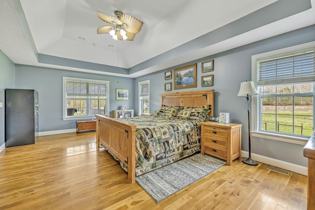 bedroom featuring multiple windows, ceiling fan, a tray ceiling, and light hardwood / wood-style flooring