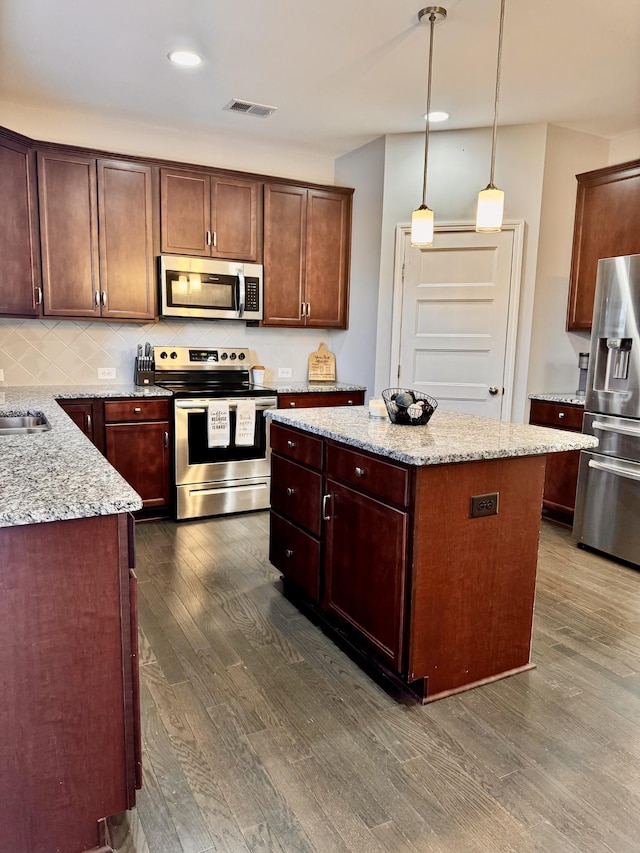 kitchen with stainless steel appliances, pendant lighting, dark wood-type flooring, light stone counters, and a kitchen island