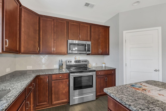 kitchen with dark wood-type flooring, stainless steel appliances, tasteful backsplash, dark stone countertops, and sink