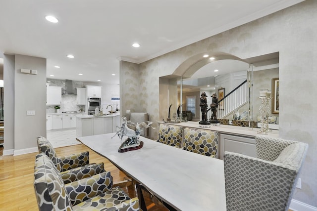 kitchen with kitchen peninsula, wall chimney exhaust hood, light wood-type flooring, backsplash, and white cabinetry