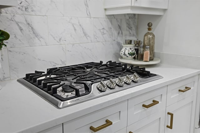 details with white cabinetry, stainless steel gas cooktop, and backsplash