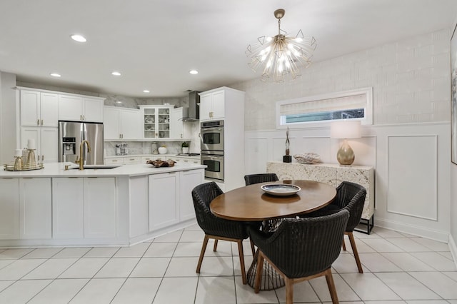 kitchen featuring white cabinets, stainless steel appliances, pendant lighting, sink, and wall chimney range hood