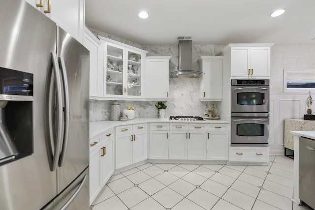 kitchen featuring appliances with stainless steel finishes, wall chimney exhaust hood, decorative backsplash, and white cabinetry