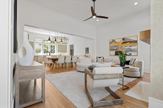 living room featuring ceiling fan with notable chandelier, light wood-type flooring, and ornamental molding