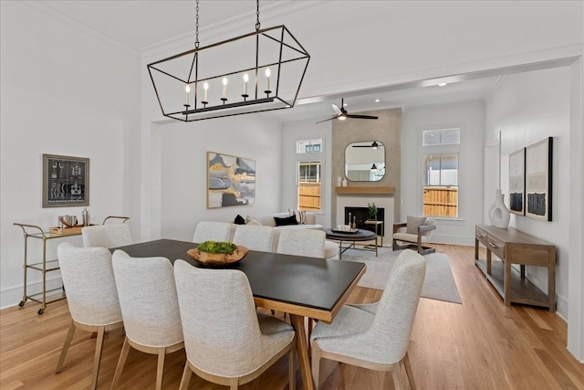 dining area featuring a large fireplace, ceiling fan with notable chandelier, a healthy amount of sunlight, and light hardwood / wood-style floors